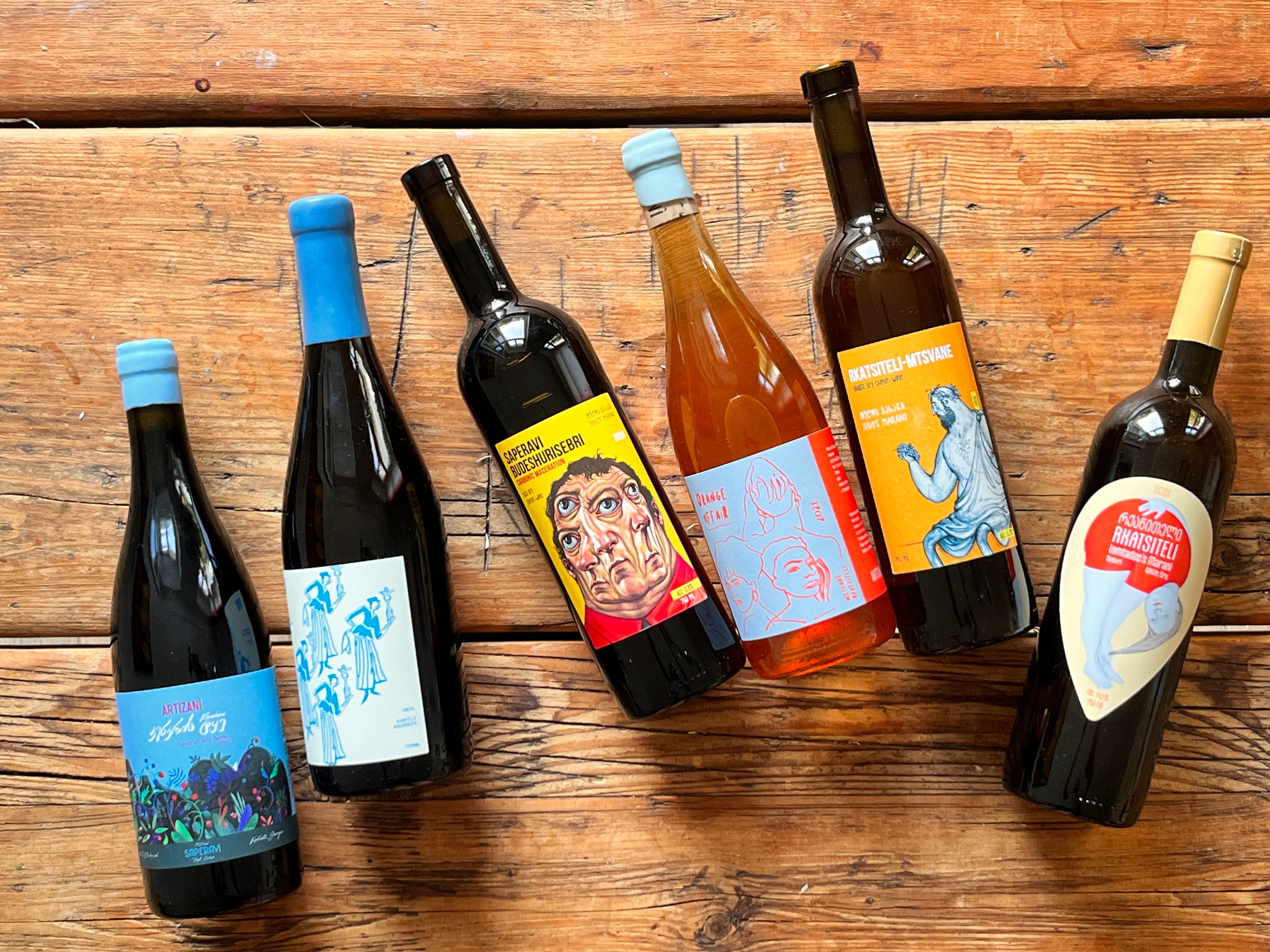 Six wine bottles with colorful labels on a wooden surface